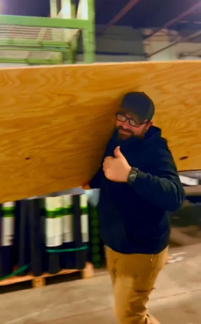 Ultimate Roofing crew member carrying plywood roof decking at the shop — Capital Region NY